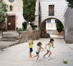 Dues nenes i un nen juguen a pilota en un carrer de vianants 